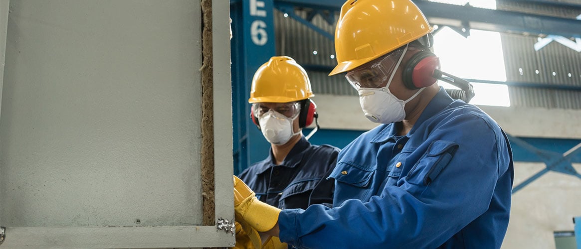 Two workers wearing personal protective equipment while insulating a pressure vessel