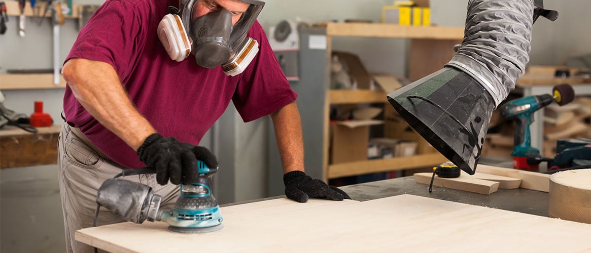 Wood worker wearing respirator and using a ventilation system to minimize wood dust exposure.