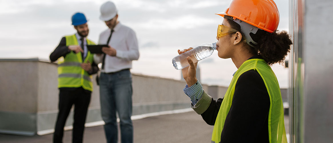 engineer drinking water on rooftop wearing helmet and safety glasses