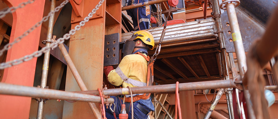 Worker at an elevation, using a fall prevention lanyard that's connected to a harness loop and attached to a structure beam
