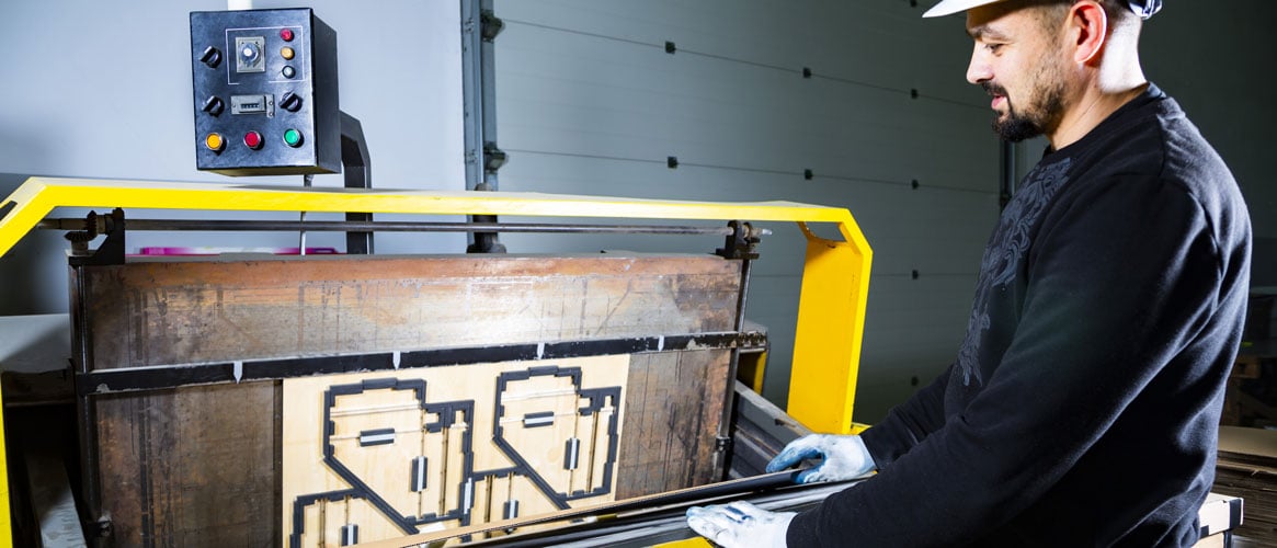 Worker in a hard hat in cardboard boxes factory placing a carton in a paper die cutting machine