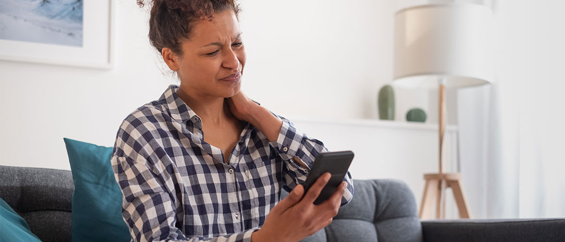 Woman suffering neck pain while using mobile device.