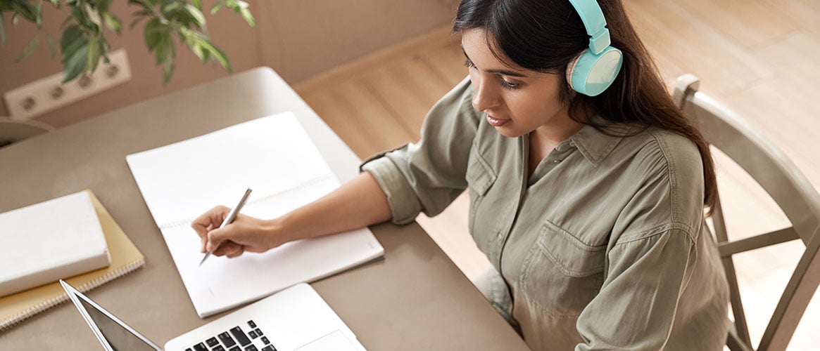 Student looking at computer, wearing headphones, learning online by attending a class webinar.