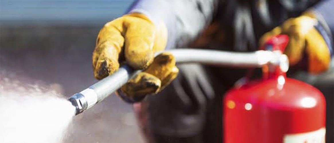 Gloved worker sprays a red fire extinguisher, highlighting workplace fire safety.
