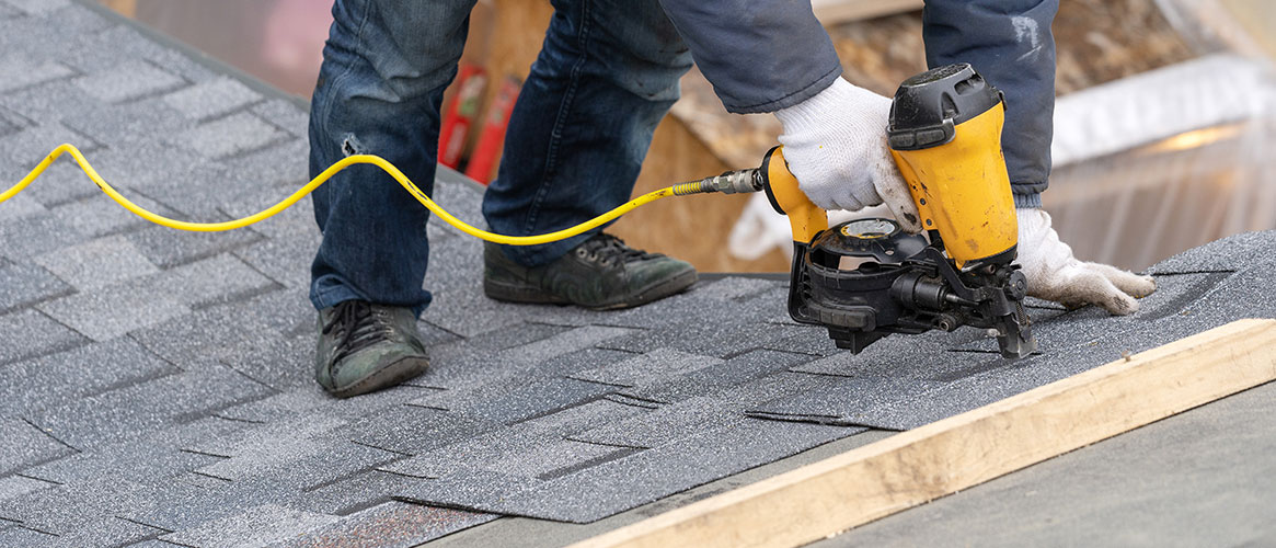 Roofer using nailgun safely with gloves on roof